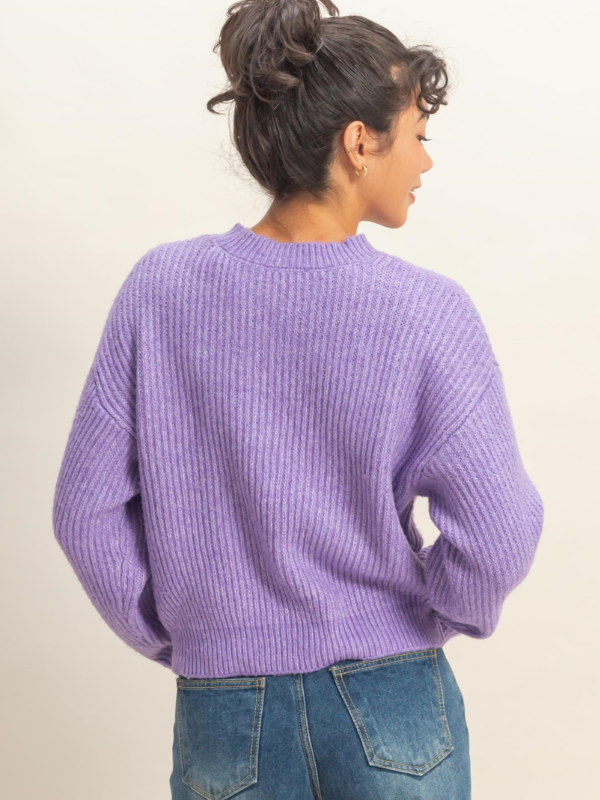 Person wearing a purple sweater and blue jeans on a plain background