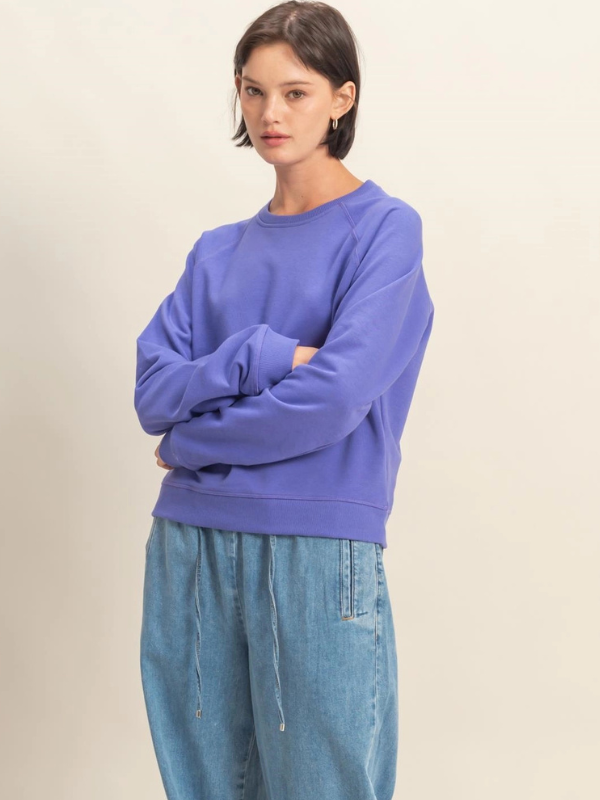 Person wearing a purple sweatshirt and blue jeans against a beige background
