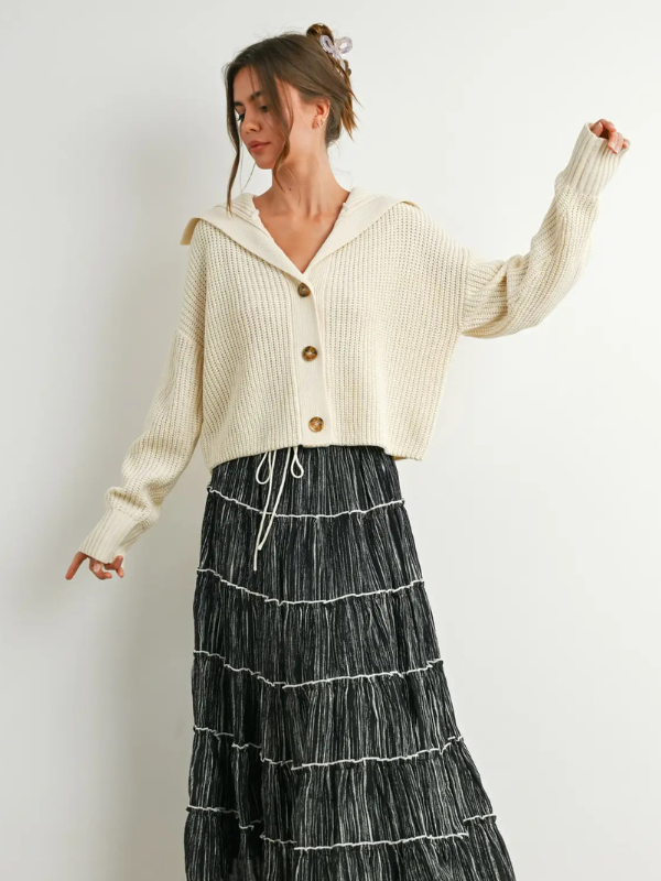 Woman wearing a cream-colored cardigan and black tiered skirt against a white background