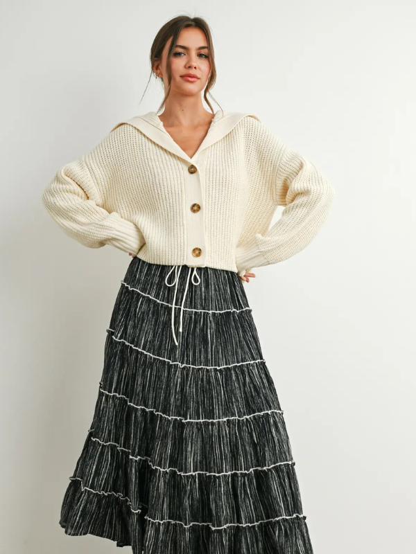 Woman wearing a cream cardigan and black tiered skirt on a white background