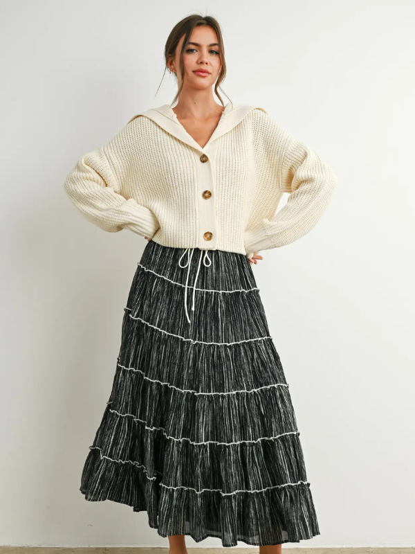 Woman wearing a cream cardigan and black tiered skirt against a white background