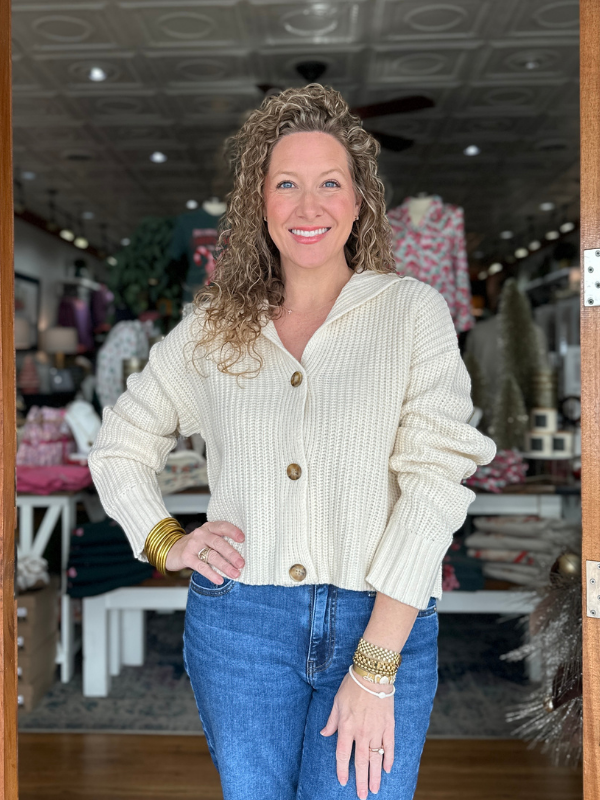Woman wearing a cream cardigan and blue jeans in a store setting