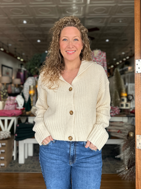 Woman wearing a cream cardigan and blue jeans in an indoor setting
