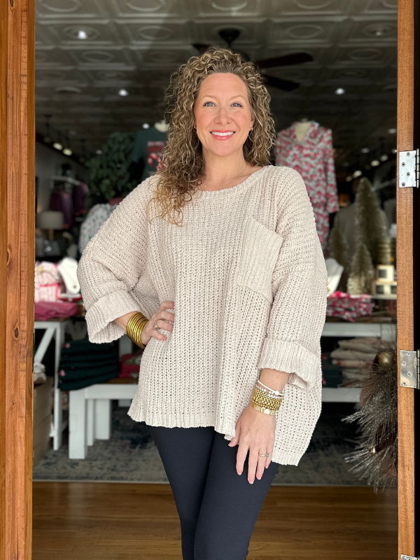 Woman wearing a beige sweater and dark pants standing in a store.