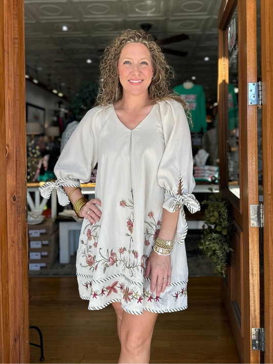 Woman wearing a white dress with floral patterns standing in a doorway.