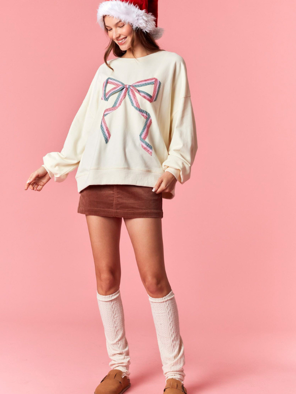Woman wearing a cream sweater with a large bow design on a pink background