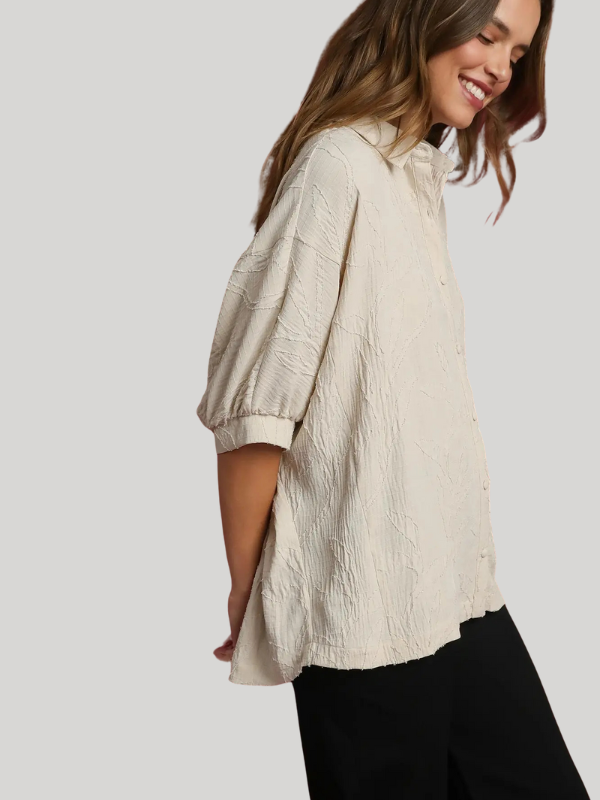 Woman wearing a textured beige blouse against a plain background