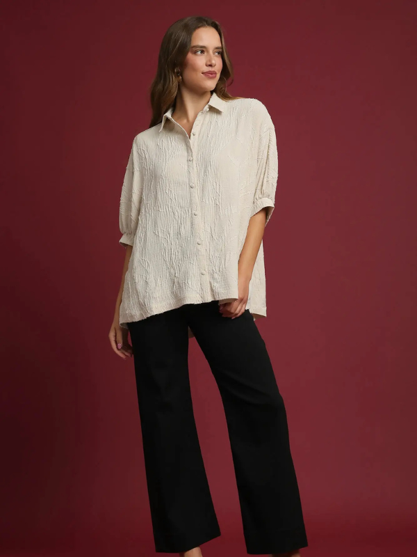 Woman wearing a beige textured shirt and black pants against a red background