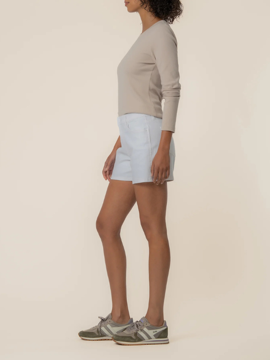 Person wearing light blue shorts and a beige top on a plain background