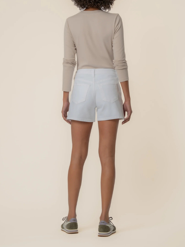 Person wearing a beige long-sleeve top and light blue shorts on a beige background