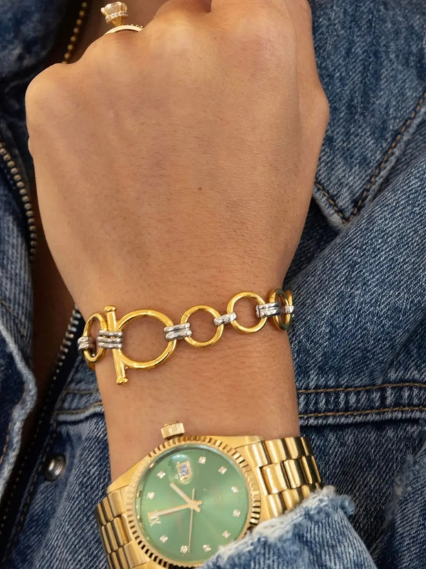 Gold bracelet and watch on a wrist with denim background