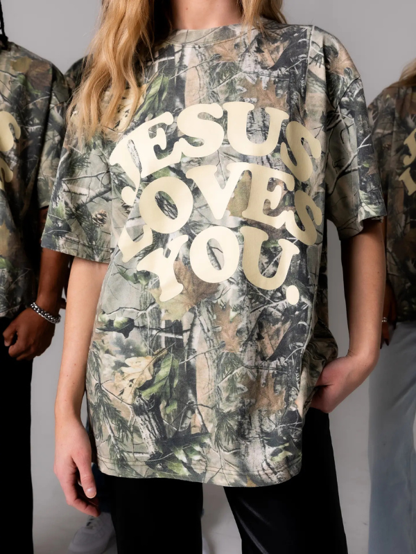 Person wearing a camouflage t-shirt with 'Jesus Loves You' text.