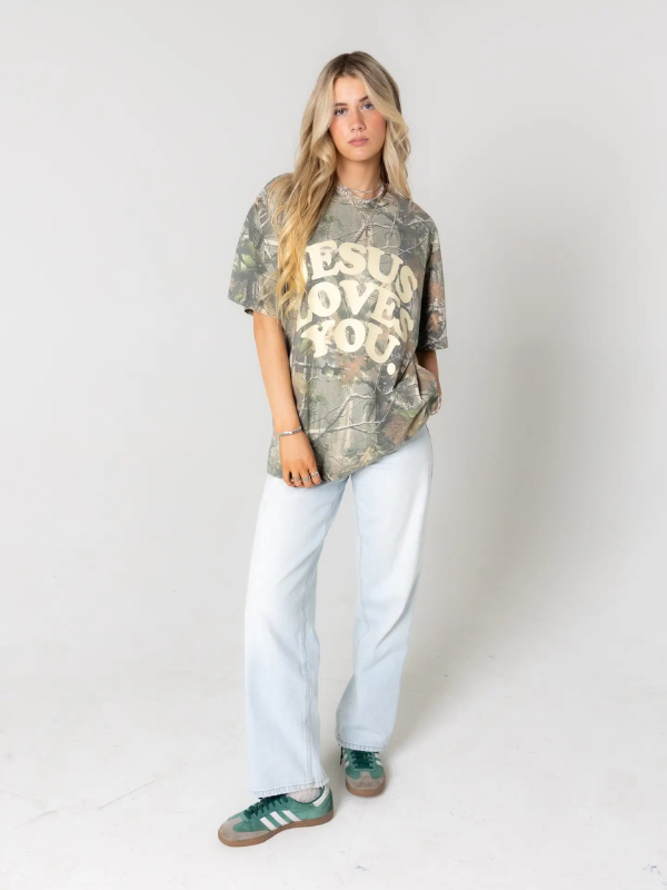 Person wearing a camouflage t-shirt with 'Jesus Loves You' text on a plain background