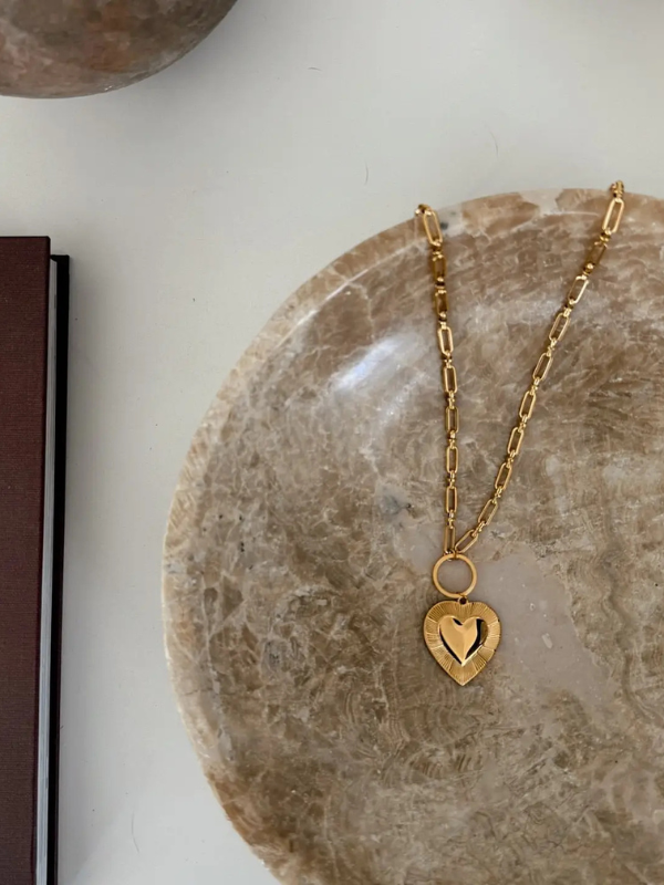 Gold chain necklace with a heart pendant on a stone surface
