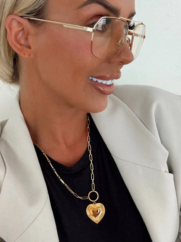 Woman wearing gold-framed glasses and a gold necklace with a heart pendant.