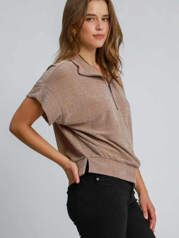 Woman wearing a brown short-sleeve top with a zipper on a plain background