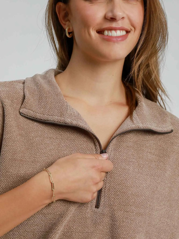 Woman wearing a beige zip-up sweater against a plain background