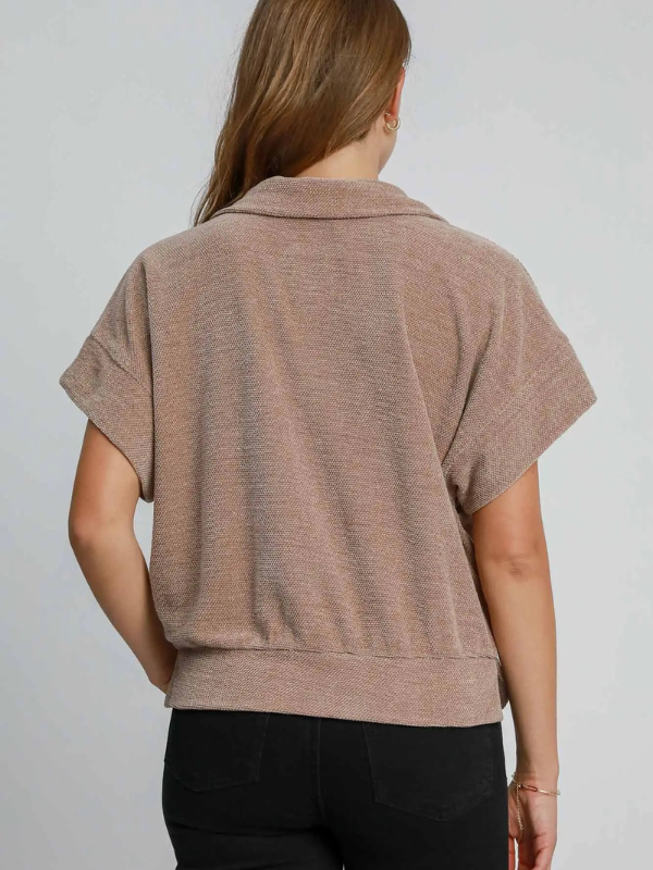 Woman wearing a brown short-sleeve top against a plain background