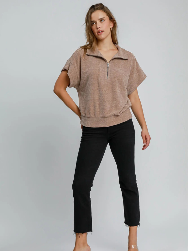 Woman wearing a brown short-sleeve top and black pants on a gray background