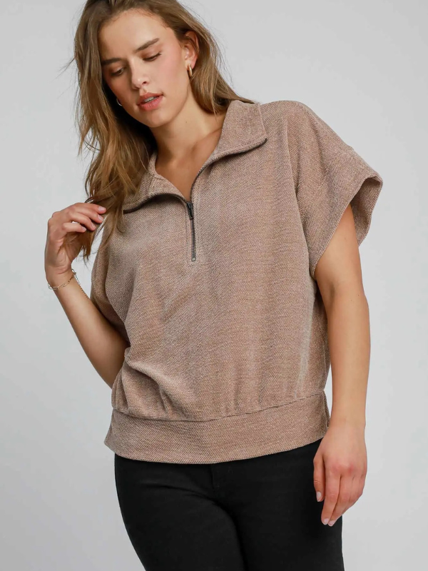 Woman wearing a beige sleeveless pullover against a plain background