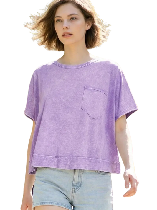 A woman wearing a lavender-purple short-sleeve crewneck t-shirt with a chest pocket, paired with light-wash denim shorts, set against a solid white background.