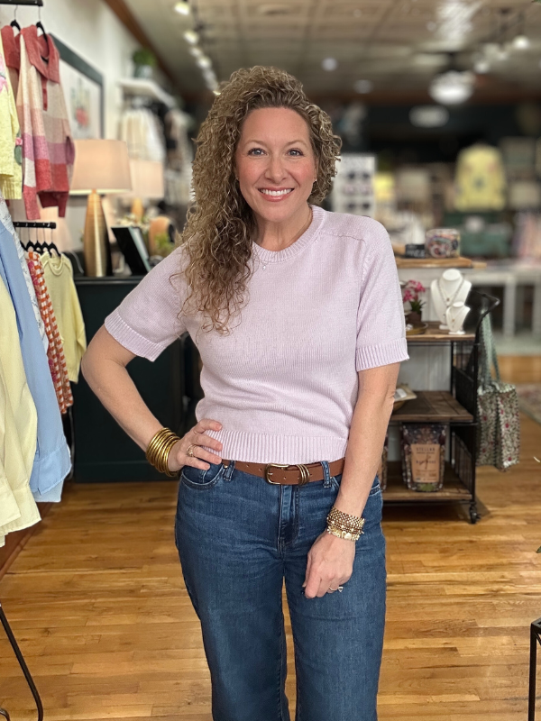 Woman wearing a light pink sweater and blue jeans in a store setting