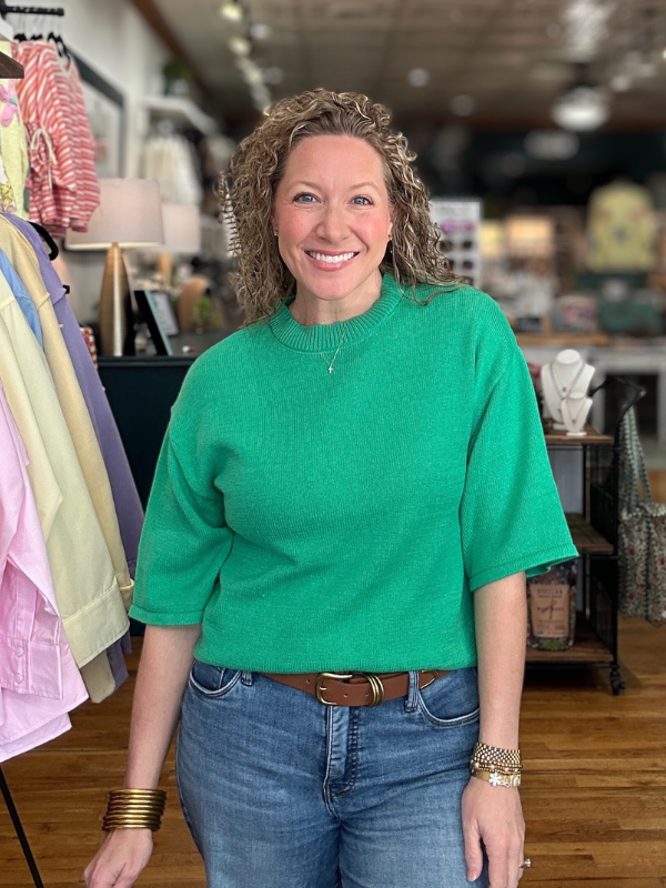 Woman wearing a green sweater and blue jeans in a store setting