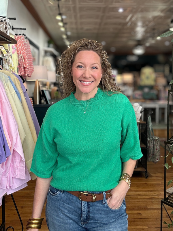 Woman wearing a green sweater and blue jeans standing in a store.