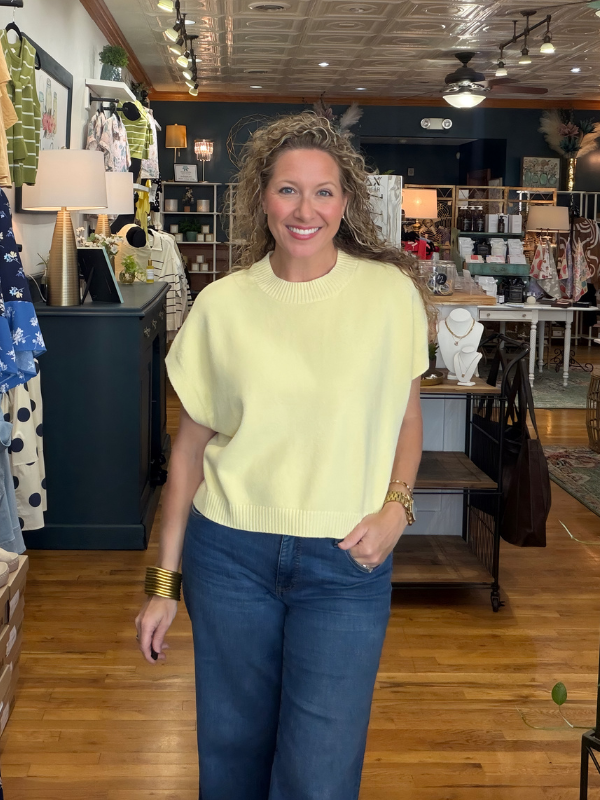 Woman in a yellow sweater and blue jeans standing in a store with various items on shelves.