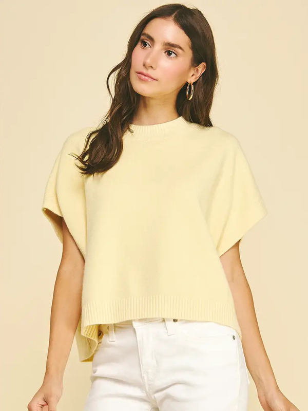 Woman wearing a light yellow sweater and white pants against a beige background
