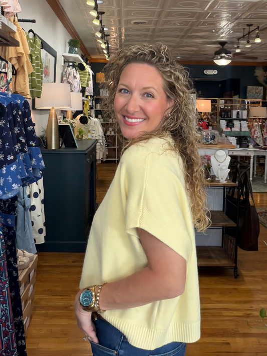 Woman in a yellow sweater standing in a store with clothing and decor items around.
