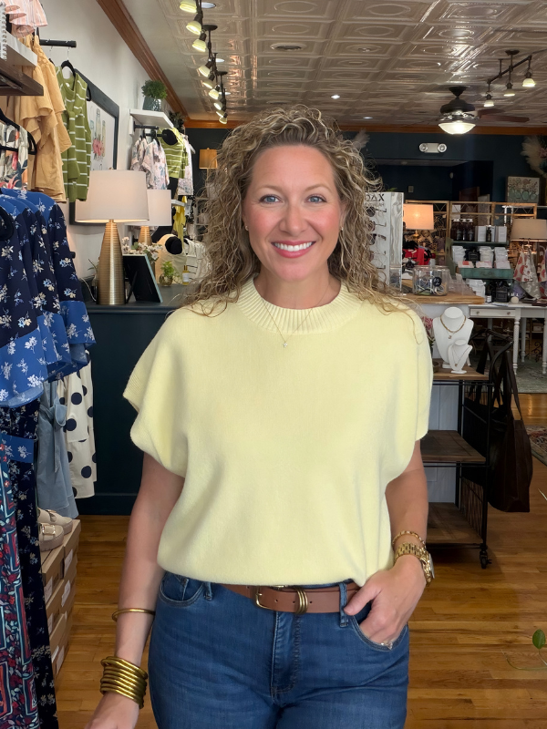 Woman in a yellow sweater and blue jeans standing in a store.