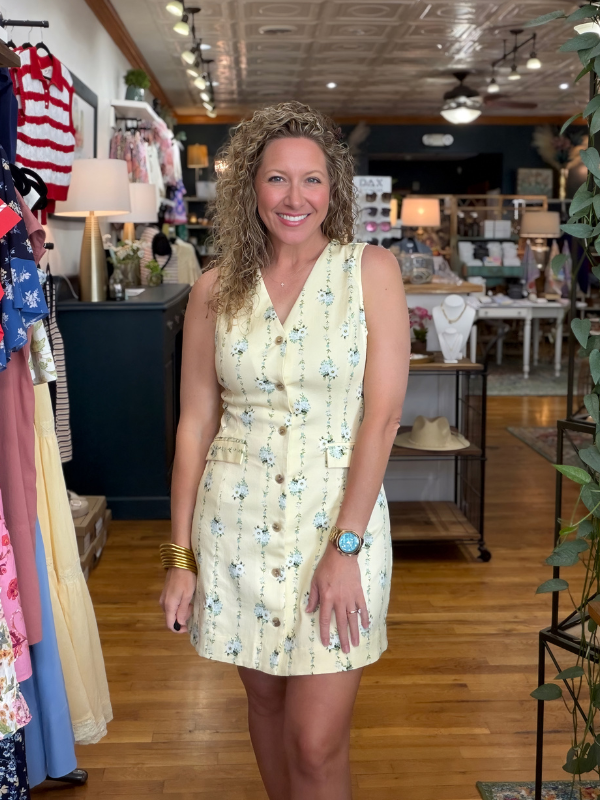 Woman in a floral dress standing in a store with clothing racks and displays.