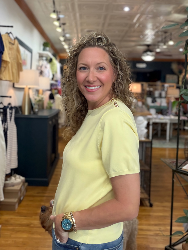 Woman in a yellow shirt standing in a store with various items in the background