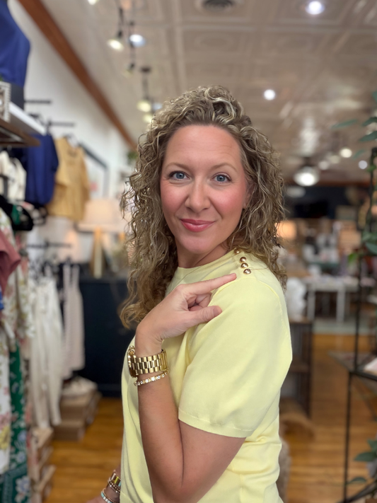 Woman in a yellow shirt pointing at herself in a store setting