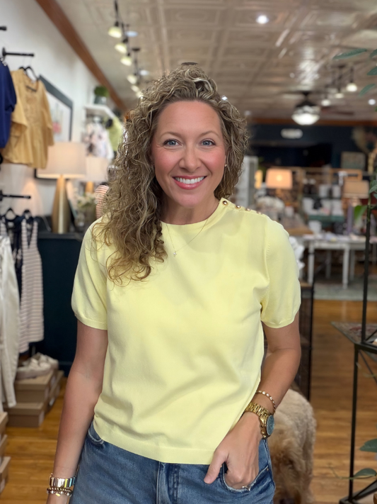 Woman in a yellow shirt standing in a store with clothing and decor items in the background