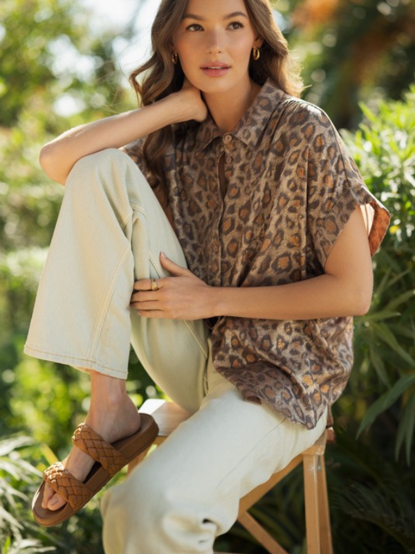 Woman wearing a leopard print poncho sitting outdoors with greenery in the background