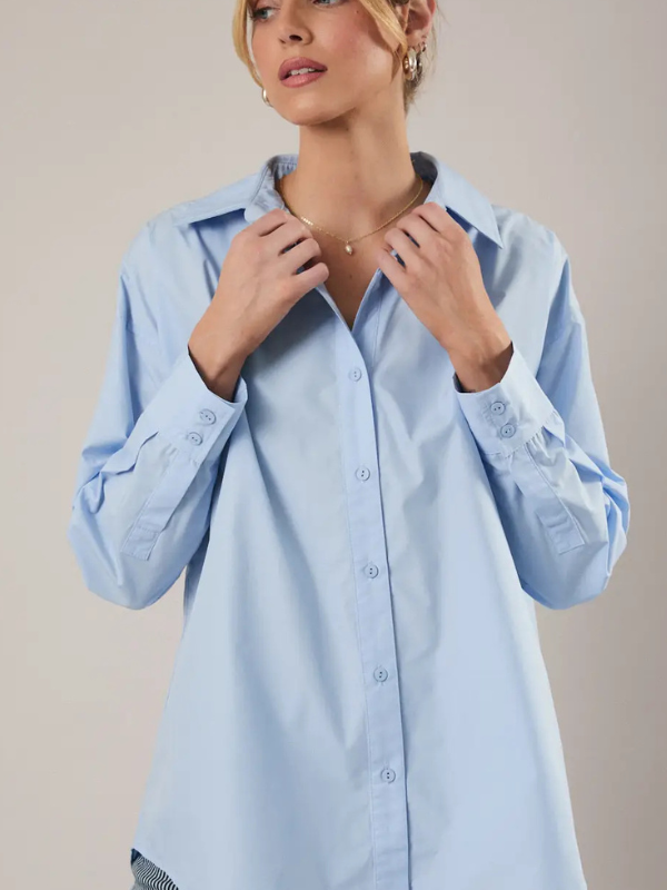 Woman wearing a light blue shirt with intricate details on a beige background