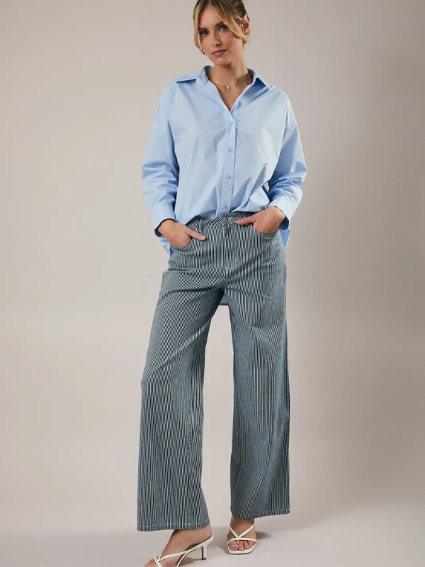 Woman wearing a light blue shirt and striped pants against a plain background