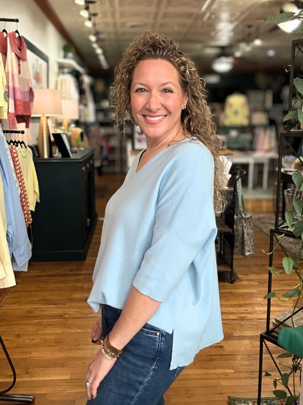 Woman in a light blue shirt and jeans standing in a clothing store.