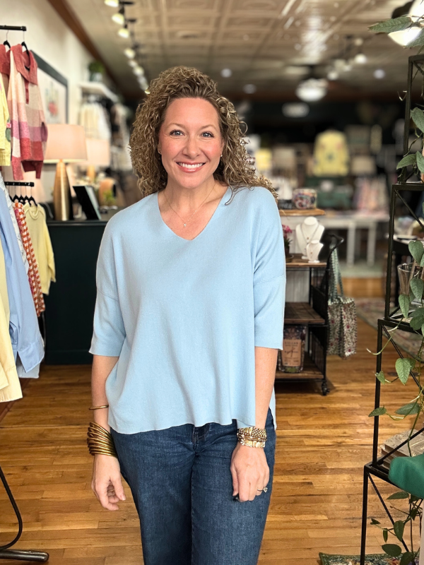 Woman wearing a light blue top and dark jeans in a store setting