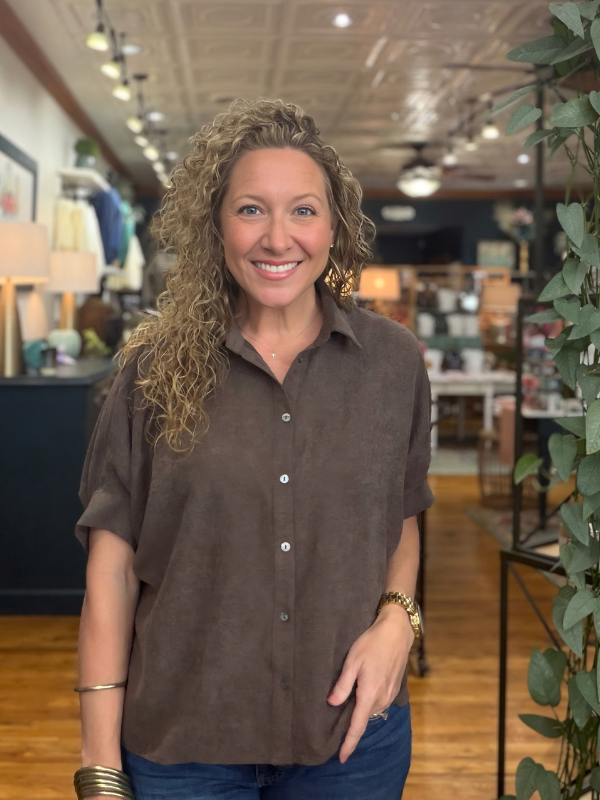A woman modeling a brown short-sleeve button-up shirt with a relaxed, oversized fit and denim jeans