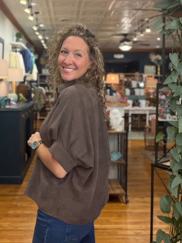 A woman modeling a brown short-sleeve button-up shirt with a relaxed, oversized fit and denim jeans