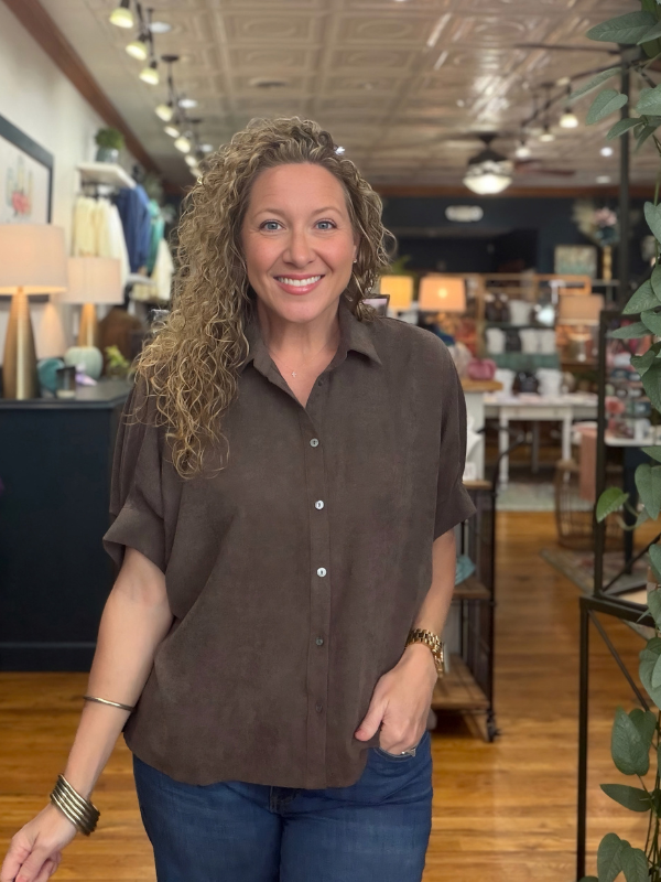 A woman modeling a brown short-sleeve button-up shirt with a relaxed, oversized fit and denim jeans
