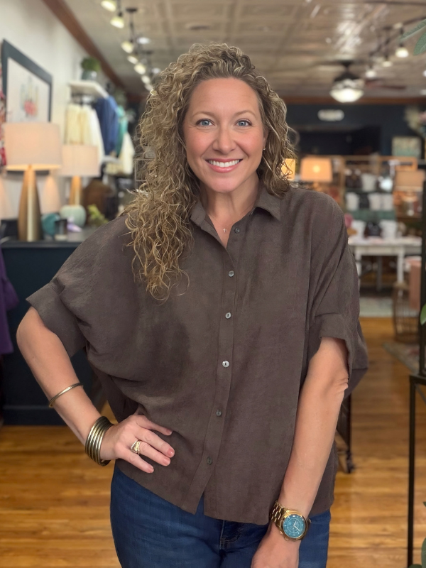 A woman modeling a brown short-sleeve button-up shirt with a relaxed, oversized fit and denim jeans