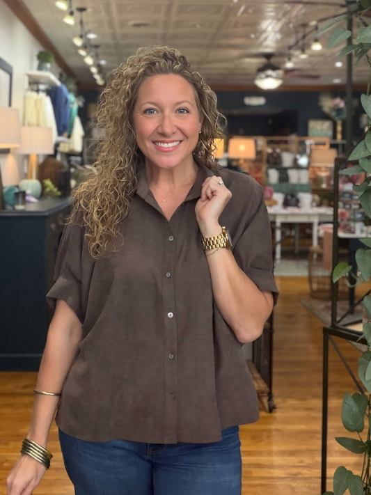 A woman modeling a brown short-sleeve button-up shirt with a relaxed, oversized fit and denim jeans