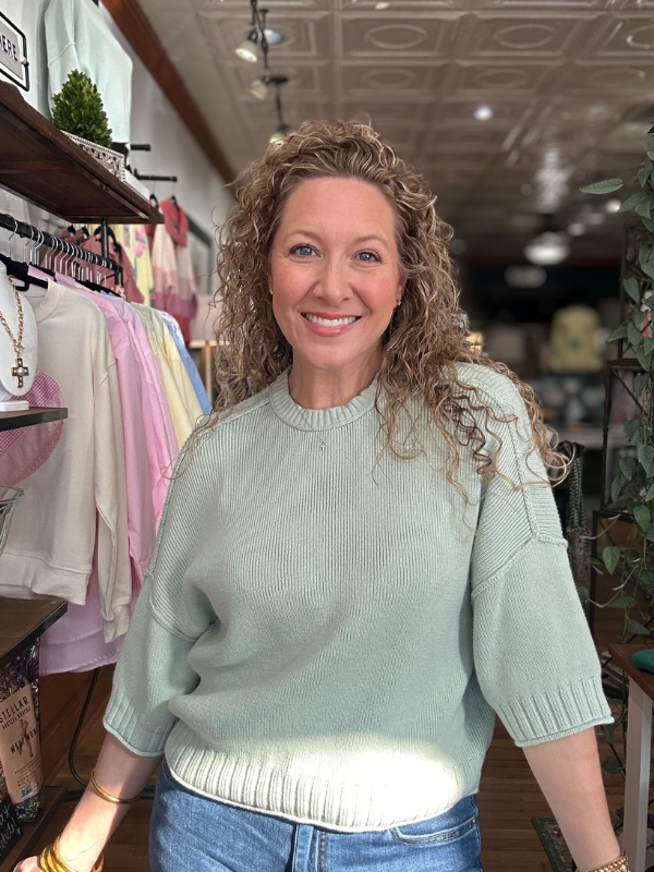 Woman wearing a light green sweater in a clothing store.