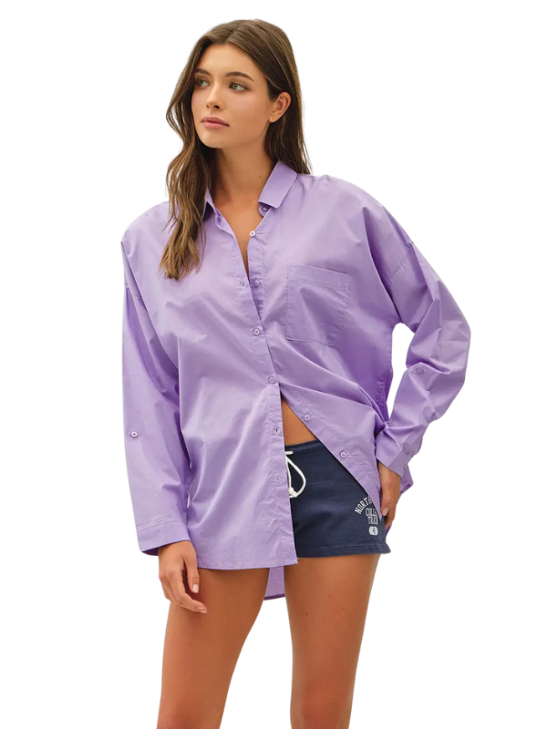 A woman modeling an oversized light purple button-up shirt paired with dark denim shorts against a plain white background.