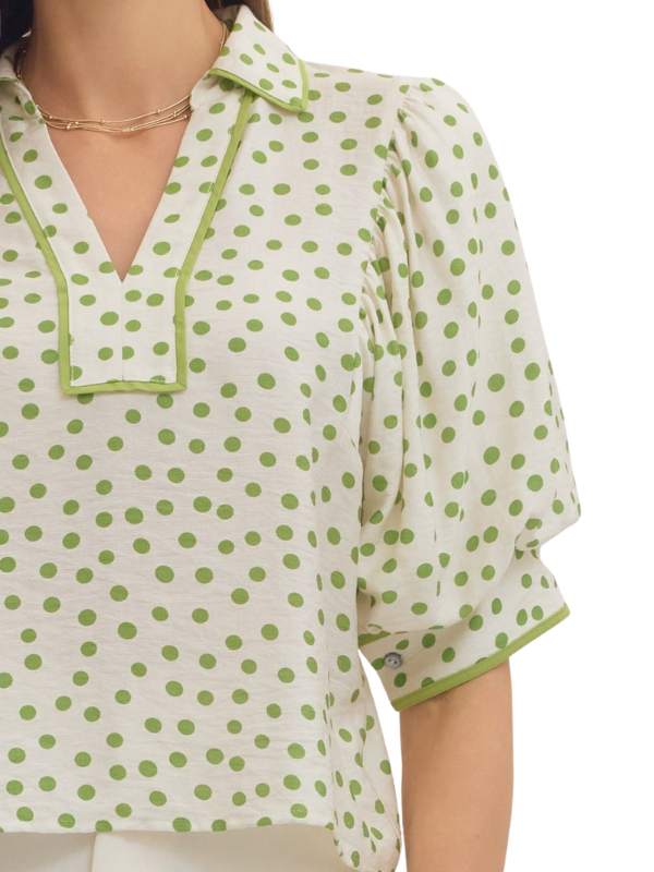 Green and white polka dot blouse on a plain background