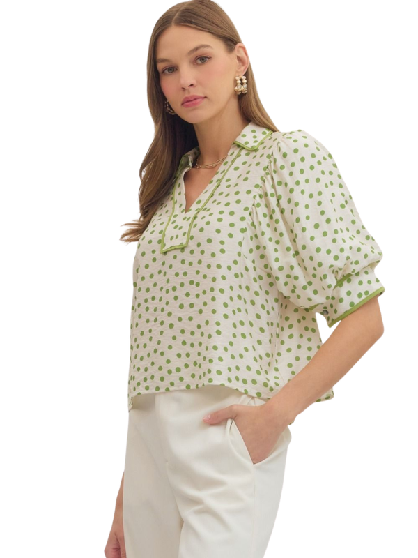 Woman wearing a green polka dot blouse with white pants on a white background